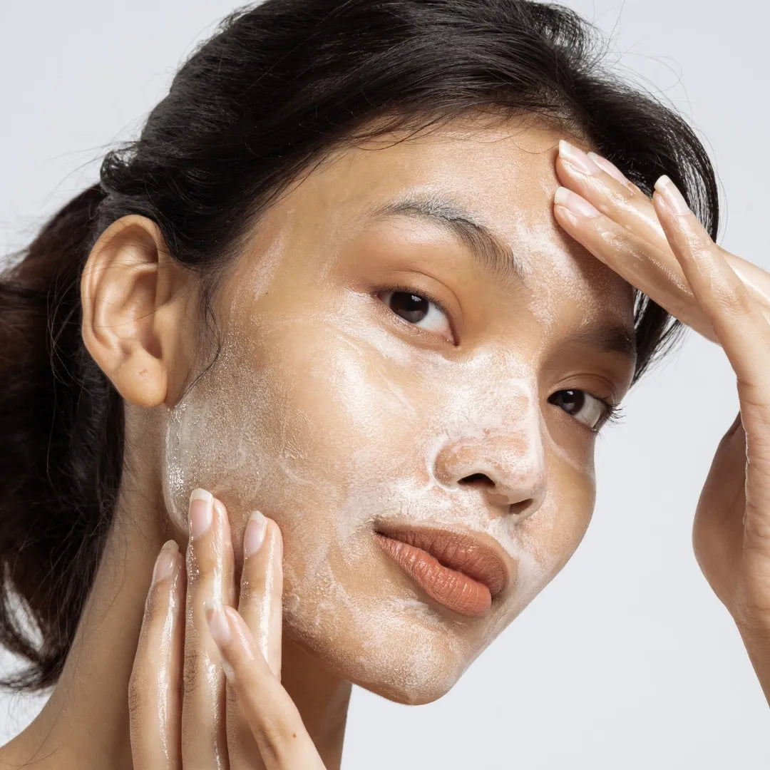 Woman massaging a white foamy cleanser onto her face.