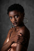 Portrait of a dark-skinned woman with short natural hair and hoop earrings, posing with her hand on her arm.