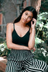 Young woman in a black top and striped pants, leaning outdoors and looking at the camera.